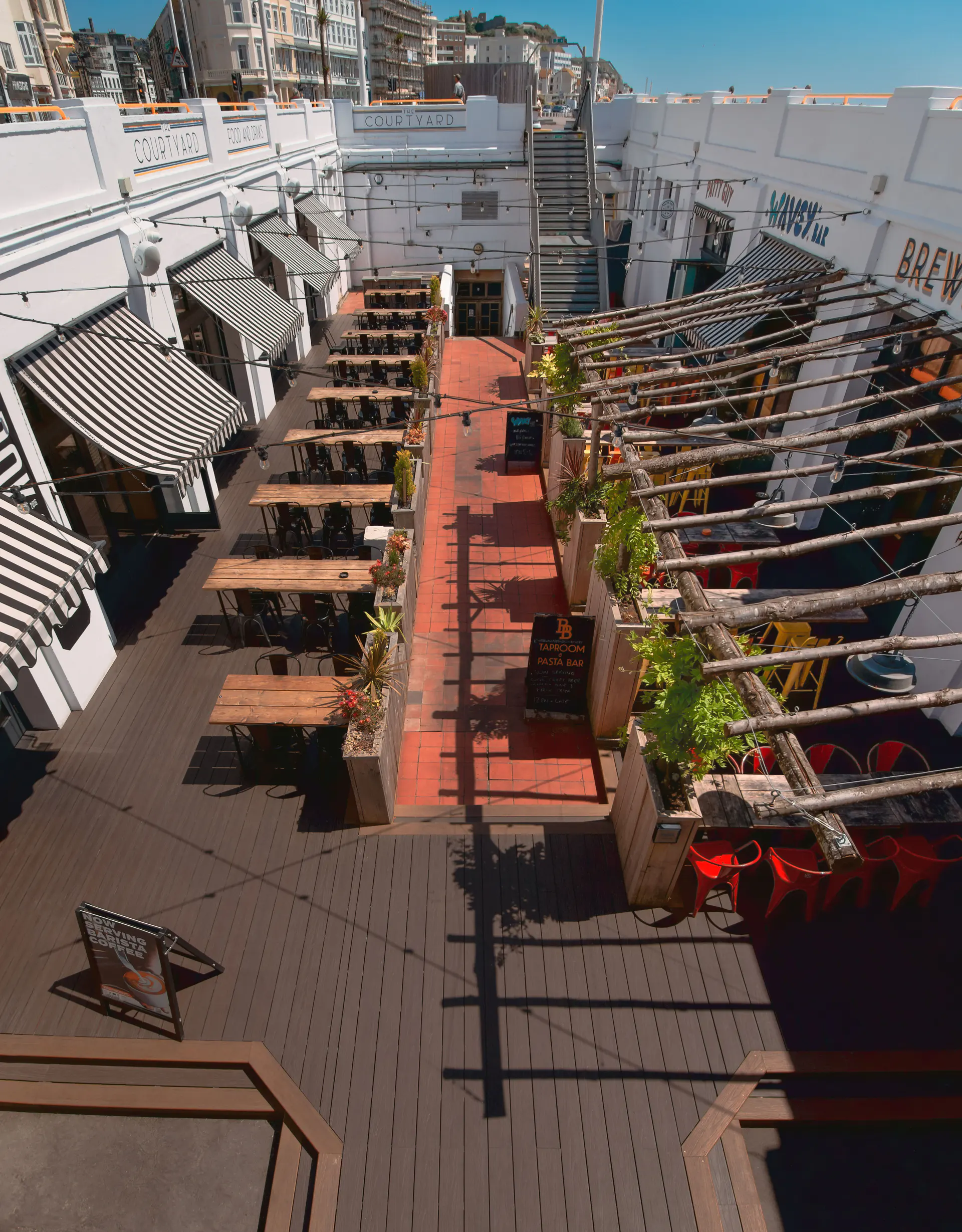 The Courtyard in Hastings with its name, full sunken dining area, wooden tables, striped awnings and central stairs