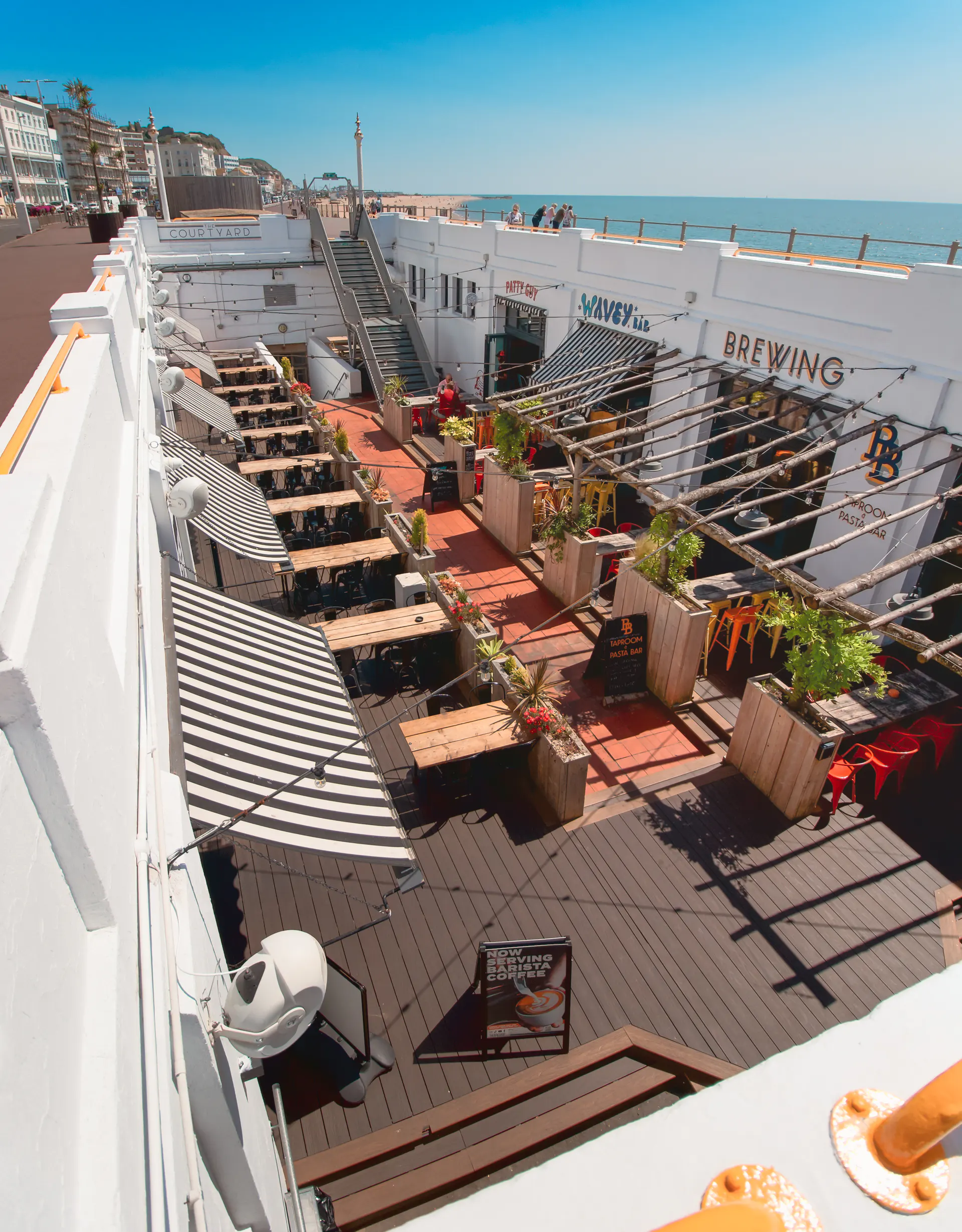 The Courtyard's dining spaces below the Hastings promenade, with the sea visible beyond the white walls